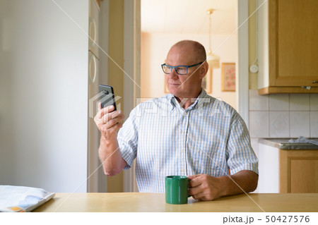 Senior Man Using Phone While Drinking Coffee By The Window 50427576