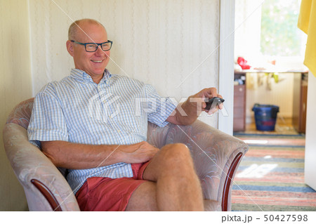 Happy Senior Man Sitting While Watching Television At Home Happy Senior Man Sitting While Watching Television At Home 50427598