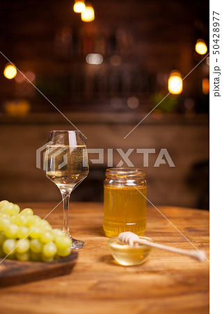 Golden honey jar next to a refined glass of white wine over a rustic table in a vintage pub 50428977