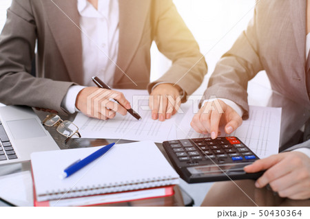 Two female accountants counting on calculator income for tax form completion hands close-up 50430364