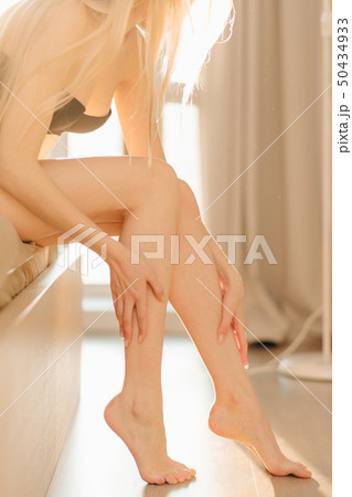 A woman in underwear with perfect fit legs sitting on bed in sunny room. A woman in underwear with perfect fit legs sitting on bed in sunny room. 50434933