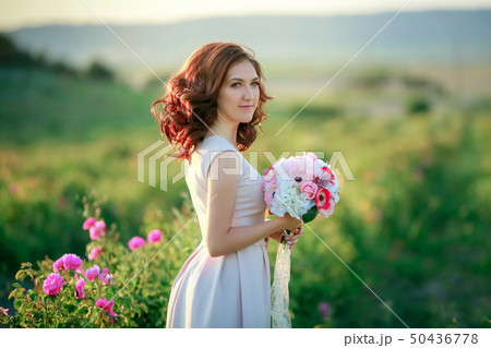 A bride in a white dress holds a bouquet of roses and callas on the background of green grass. A bride in a white dress holds a bouquet of roses and callas on the background of green grass. 50436778