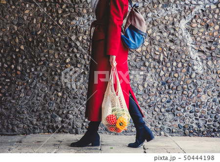 Style woman in red coat and net bag waking home after shopping. 50444198