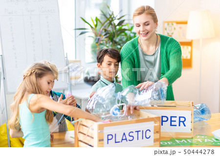 Teacher and children putting plastic bottles into box while sorting waste 50444278