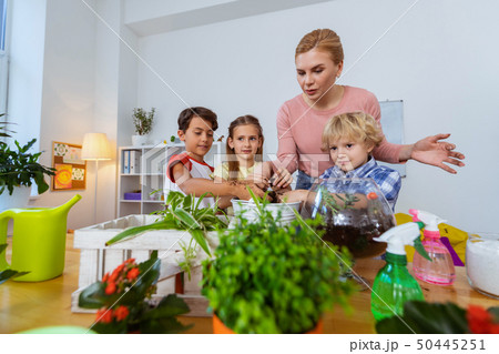 Three pupils and their teacher standing near table with plants 50445251