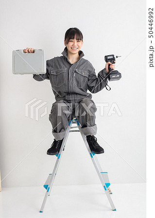 白背景スタジオ撮影作業服をきた女の子がドライバーを持って脚立に乗っている作業をしている全身工業女子 50446992
