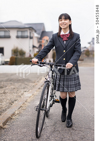 髪の毛が長い女子高生が制服を着て夕焼けに向かって自転車で歩く姿帰宅部の写真素材