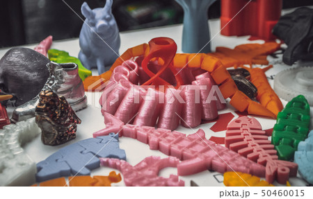 Many bright multi-colored objects printed on 3d printer lie on flat surface 50460015