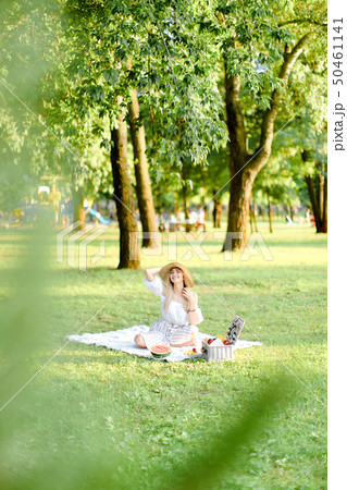 Young european woman in hat resting on plaid with fruits in park. 50461141