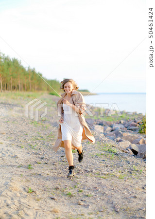 Young pretty woman walking on shingle beach and wearing summer coat. 50461424