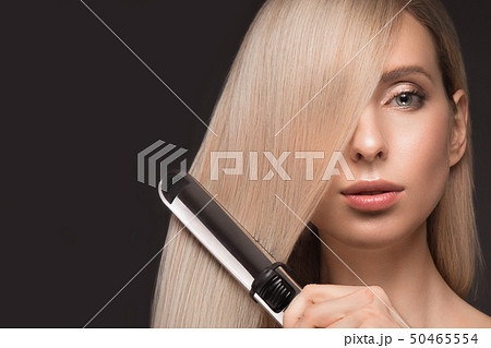 Beautiful blond girl with a perfectly smooth hair, classic make-up with curling styler in the hands. Beautiful blond girl with a perfectly smooth hair, classic make-up with curling styler in the hands. 50465554