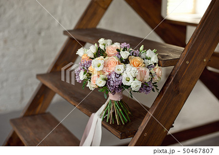 Beautiful bouquet of flowers of roses and lilac stands on a wooden ladder against a white brick wall Beautiful bouquet of flowers of roses and lilac stands on a wooden ladder against a white brick wall 50467807