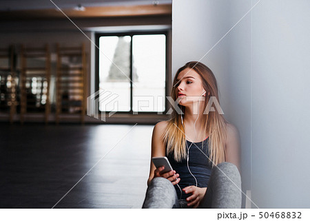 A young girl or woman with earphones and smartphone in a gym. 50468832
