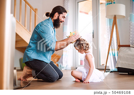 Side view of small girl with a princess crown and young father at home, playing. Side view of small girl with a princess crown and young father at home, playing. 50469108