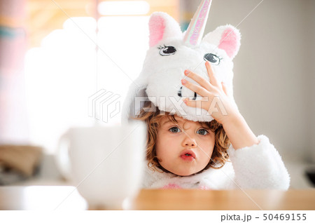 A portrait of small girl in unicorn mask sitting at the table at home. A portrait of small girl in unicorn mask sitting at the table at home. 50469155