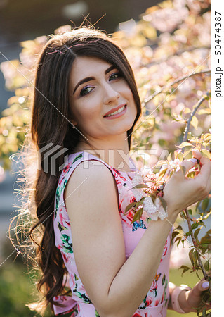 Elegant woman in beautiful dress stand by the pink tree in the park Elegant woman in beautiful dress stand by the pink tree in the park 50474387