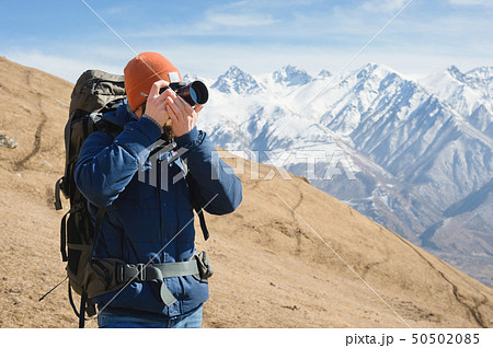 Portrait of a bearded male photographer in sunglasses and a warm jacket with a backpack on his back 50502085