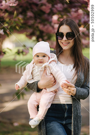 Beautiful mom walk with her baby girl on hands in the park. Pink background Beautiful mom walk with her baby girl on hands in the park. Pink background 50502999