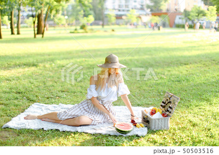 Young beautiful gitrl sitting in park on plaid near fruits, grass in background. Young beautiful gitrl sitting in park on plaid near fruits, grass in background. 50503516