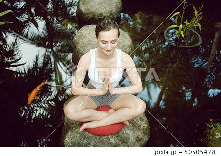 Woman doing yoga at a pond with gold fish 50505478