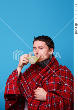 A wrapped in a blanket sick man is drinking from cup of medicine. A wrapped in a blanket sick man is drinking from cup of medicine. 50505954