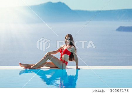 Young woman in a red swimsuit sitting by the pool 50507178