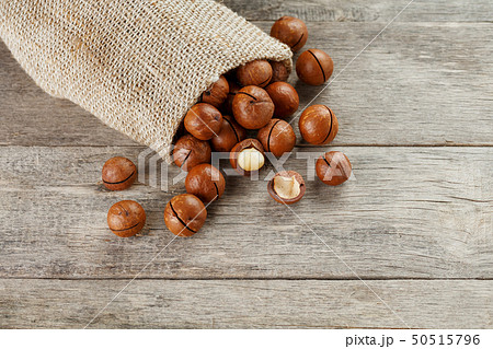 Macadamia nuts spilled out of the bag on a wooden 50515796