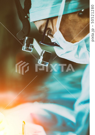 Surgeon performing surgery in hospital operating room. Surgeon in mask wearing loupes during medical Surgeon performing surgery in hospital operating room. Surgeon in mask wearing loupes during medical 50521280