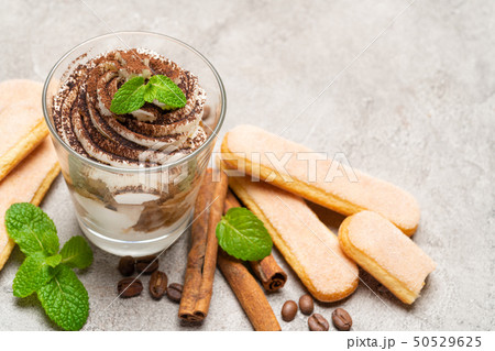 Classic tiramisu dessert in a glass and savoiardi cookies on concrete background Classic tiramisu dessert in a glass and savoiardi cookies on concrete background 50529625