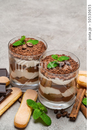 Classic tiramisu dessert in a glass and savoiardi cookies on concrete background Classic tiramisu dessert in a glass and savoiardi cookies on concrete background 50530655
