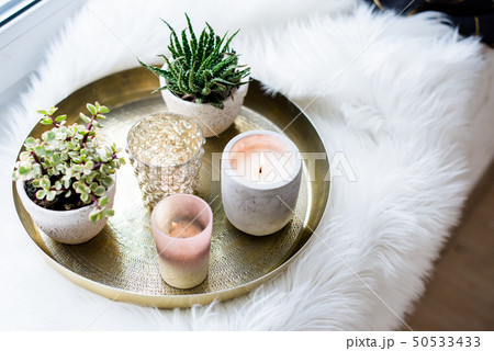 Cozy real home decoration, burning candles on golden tray with pillow on white faux fur on 50533433
