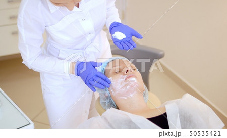 concept beautician. The hands of a cosmetologist put cream on the face of a woman. Beautician 50535421