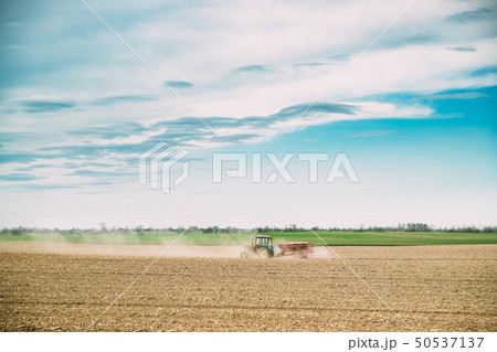 Tractor with Seeder In Dusty Field In Spring Season. Beginning Of Agricultural Spring Season Tractor with Seeder In Dusty Field In Spring Season. Beginning Of Agricultural Spring Season 50537137