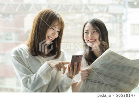 窓辺でスマホと新聞を見る女性二人 50538147