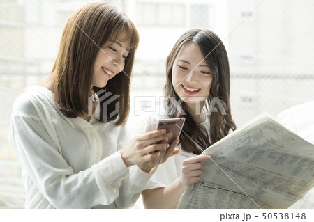 窓辺でスマホと新聞を見る女性二人 50538148