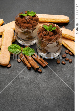 Classic tiramisu dessert in a glass and savoiardi cookies on dark concrete background Classic tiramisu dessert in a glass and savoiardi cookies on dark concrete background 50555847