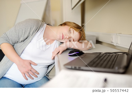 Tired pregnant woman sleeping near laptop at her Tired pregnant woman sleeping near laptop at her 50557442