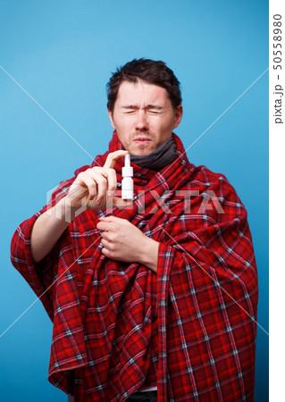 A wrapped in a blanket sick man is standing with nasal spray in his hand 50558980