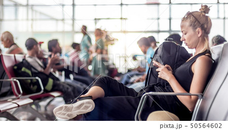 Female traveler using her cell phone while waiting to board a plane at departure gates at asian 50564602