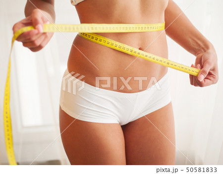 Slim young woman measuring her thin waist with a tape measure 50581833