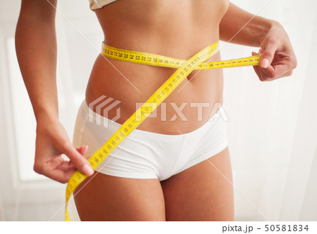 Slim young woman measuring her thin waist with a tape measure 50581834
