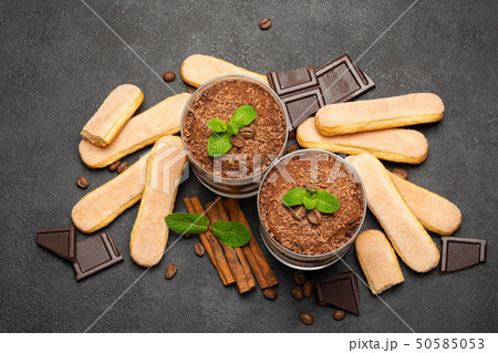 Classic tiramisu dessert in a glass and savoiardi cookies on dark concrete background Classic tiramisu dessert in a glass and savoiardi cookies on dark concrete background 50585053