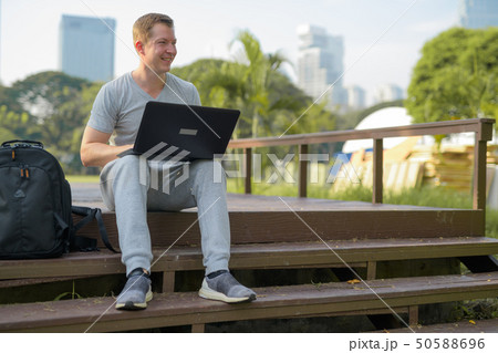 Young happy man thinking while using laptop on wooden bridge at the park Young happy man thinking while using laptop on wooden bridge at the park 50588696