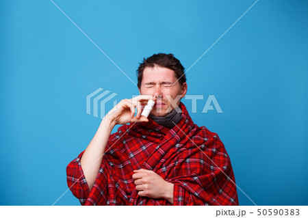 A wrapped in a blanket sick man is standing and using nasal spray 50590383