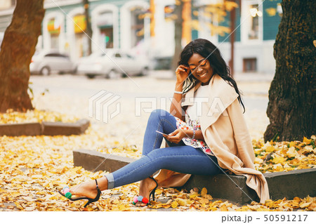 Black woman sitting in a autumn city Black woman sitting in a autumn city 50591217