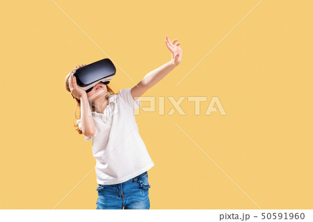 Girl 7 y.o. experiencing VR headset game on yellow background. Surprised emotions on her face.Child 50591960