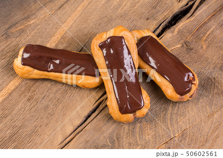Eclairs with chocolate topping on wood background. Eclairs with chocolate topping on wood background. 50602561