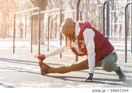 Sports girl in warm clothes on a sunny day does a warm-up on the outdoor sports field in the winter Sports girl in warm clothes on a sunny day does a warm-up on the outdoor sports field in the winter 50607204