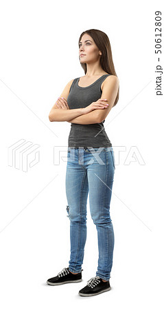 Young woman in gray top and blue jeans standing in half-turn with arms folded, looking up and away Young woman in gray top and blue jeans standing in half-turn with arms folded, looking up and away 50612809