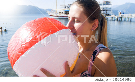 Closeup photo of young woman inflating colorful beach ball with mouth Closeup photo of young woman inflating colorful beach ball with mouth 50614996